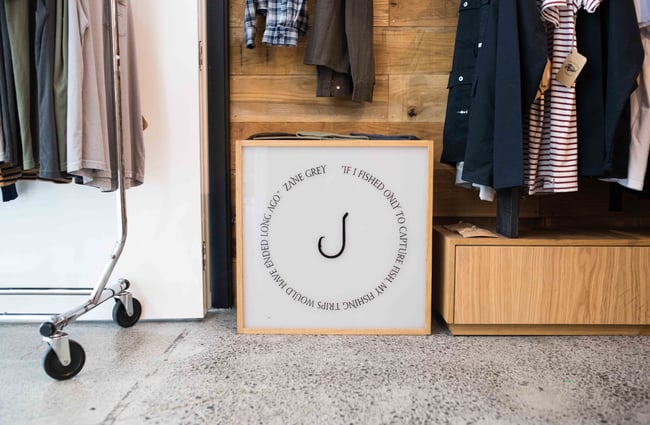 Black and white fishing hook sign on floor by clothing racks.
