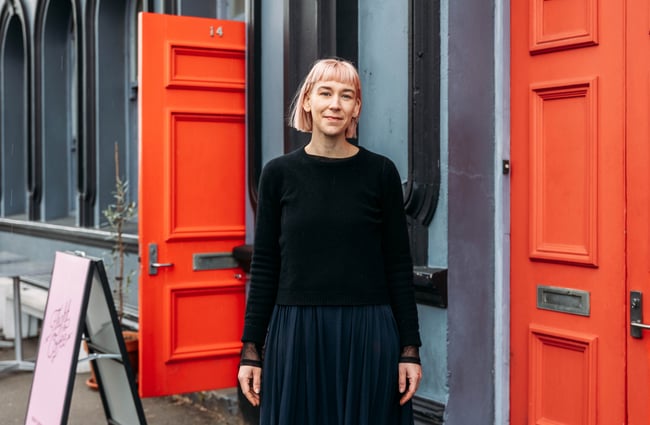 A woman with a blunt hair cut posing for camera outside a large grey building.