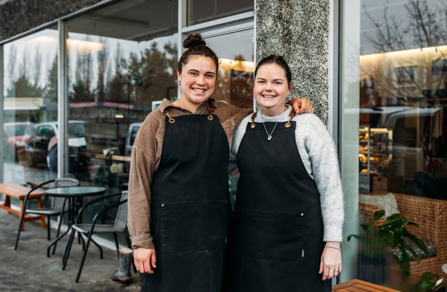 Two women wearing aprons smiling to camera.