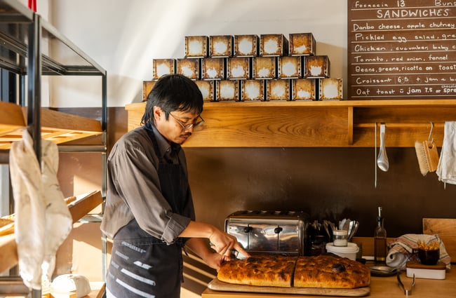 A staff member cutting focaccia inside Florets Auckland.