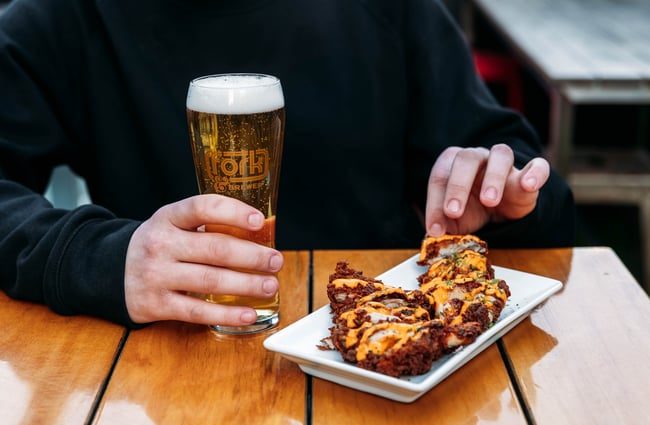 Customer holds a pint of beers and picks up a piece of fried chicken at Fork & Brewer.