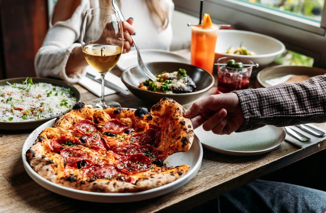 Customer takes a slice of pizza and another customer has a plate of pasta in the background at Francesca.
