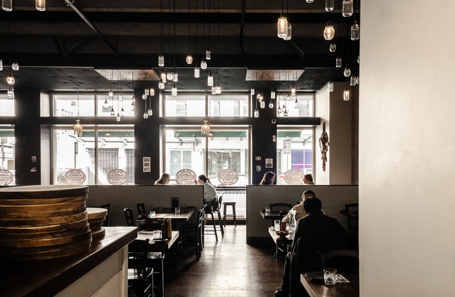 Customers dining inside a dimly lit restaurant with large glass windows in the background.