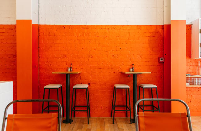 Stools at leaner table against an orange wall at Fred's, Wellington.