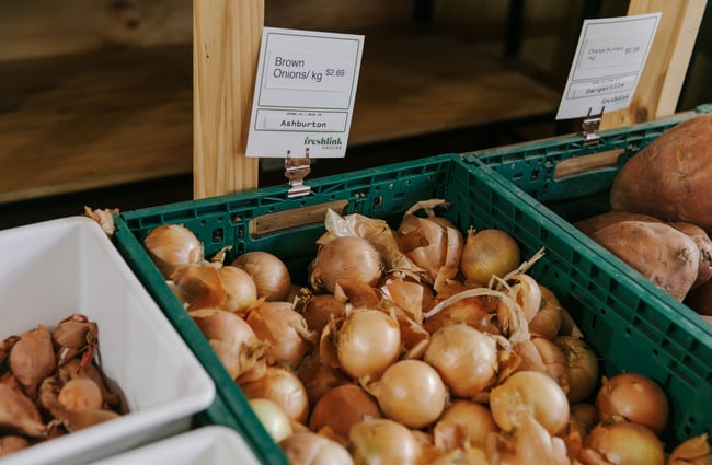 Green produce tubs filled with yellow onions and orange kumara.