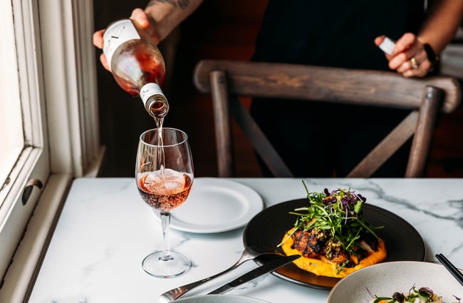 Food dish on the table and a glass of wine being poured at Gear Homestead.