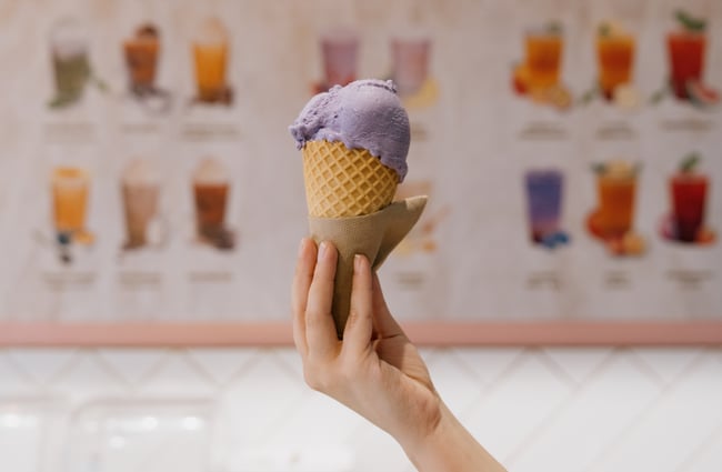 Person holding up scoop of purple ube ice cream in a cone