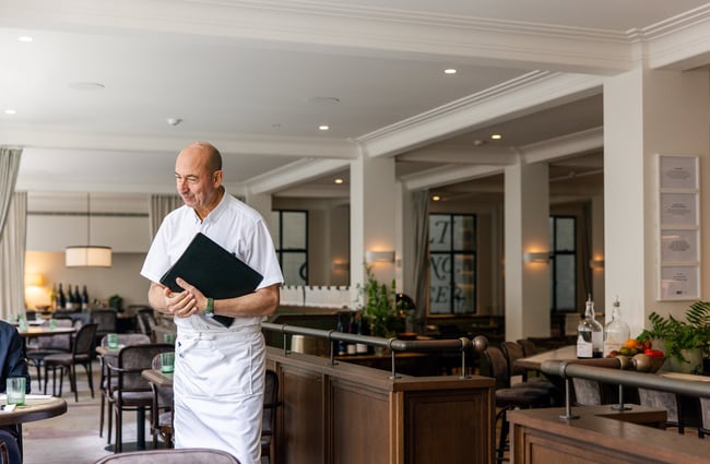 Man in white uniform serving customers at Gilt Brasserie in Auckland