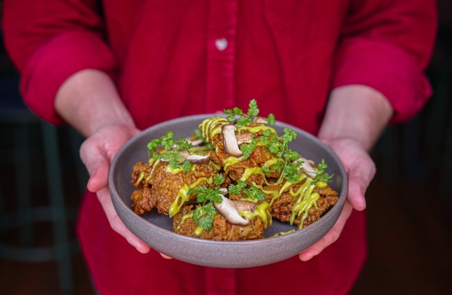 Person holding a shallow bowl of fried chicken with shiitake mushrooms and a green sauce at gin gin.
