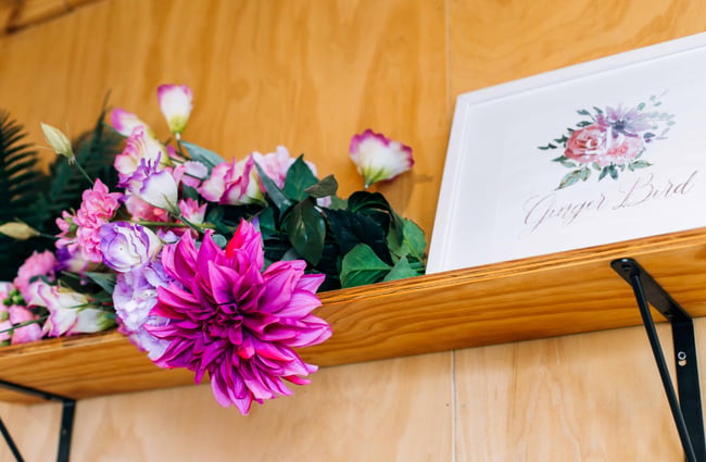 Close up of a purples flower hanging down off a wooden shelf.