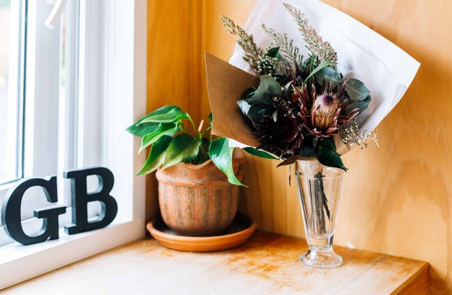 Dried flowers in a glass vase on a wooden table with a plant next to it.