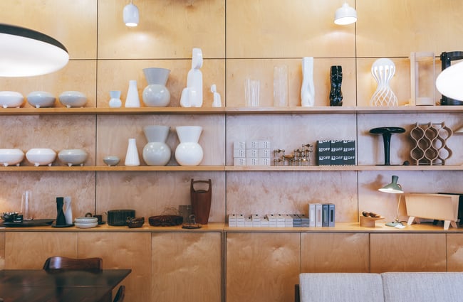 Floating shelves on a plywood wall displaying grey and white vases.