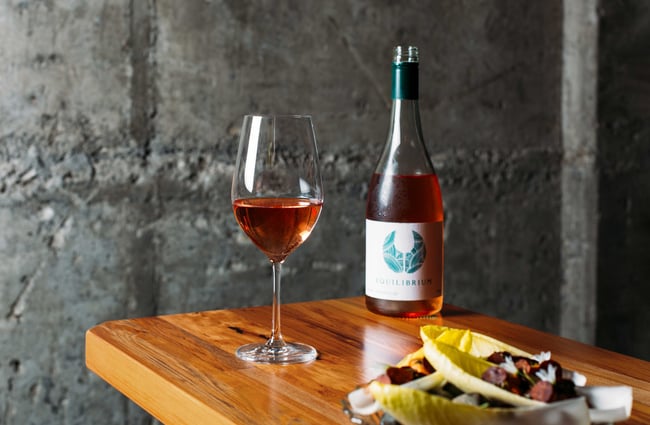 A close up of a glass of wine, a wine bottle and a plate of food on a table.