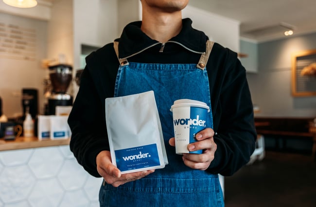 Close up of a staff member in an apron holding a bag of Grey Roasting Co. coffee beans.