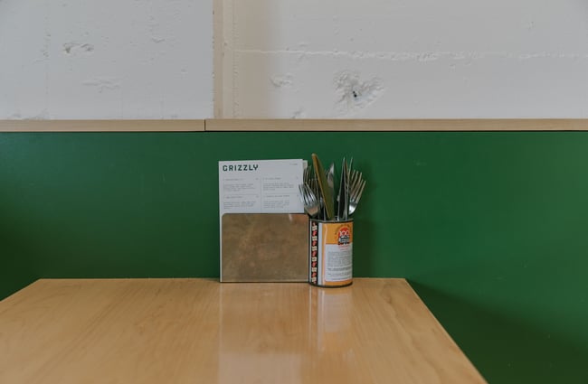 Menus in a stand and cutlery in a tin on a table at Grizzly Baked Goods in the Christchurch CBD.