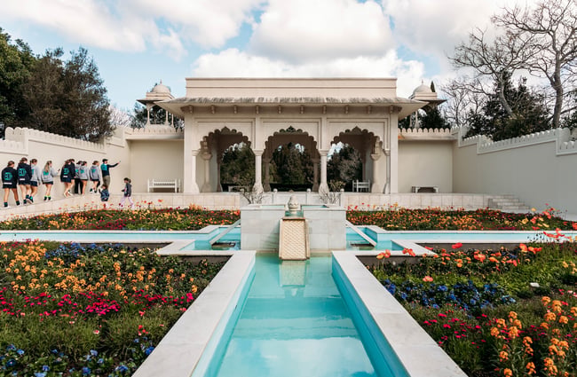 A water feature surrounded by colourful flowers in front of an Indian-style pavilion.
