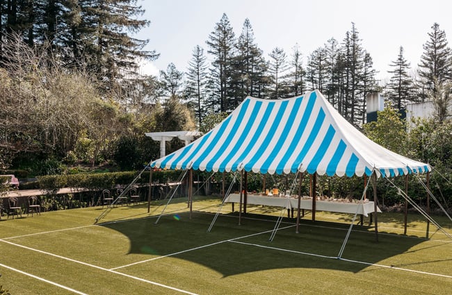 A blue and white striped canopy pitched on the side of an artificial turf tennis court.