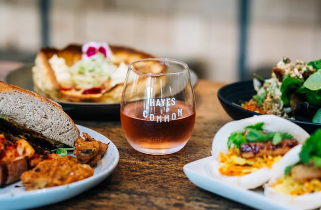 A glass of rosé and plates of food on a table at Hayes Common, Hamilton.