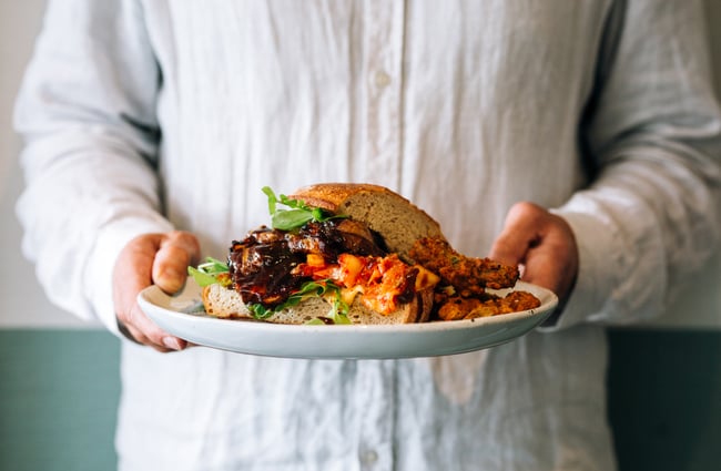Two hands hold a plate with a colourful sandwich on it at Hayes Common, Hamilton.