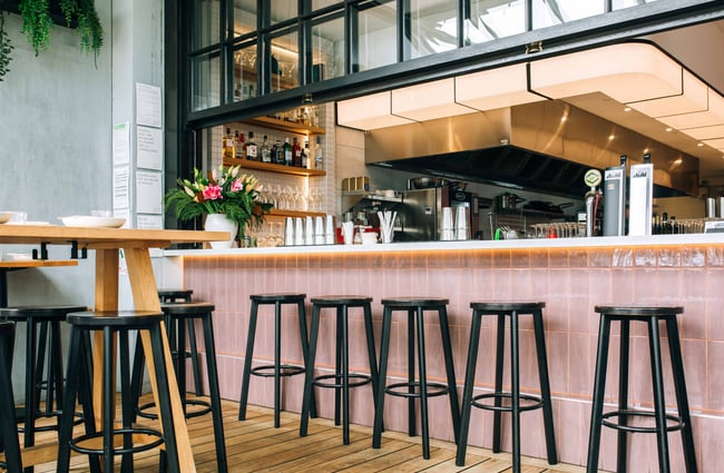 Black stools lined up next to pink tiles at Hello Beasty, Auckland Viaduct Harbour.