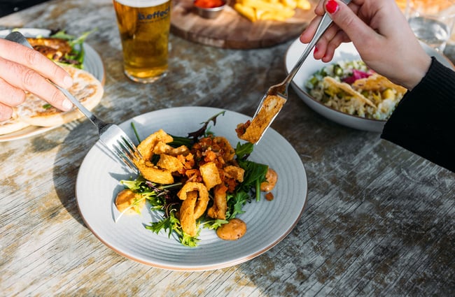 Two hands holding forks reach for fried calamari from a plate in the middle of a table at hello RANGER, Wānaka.