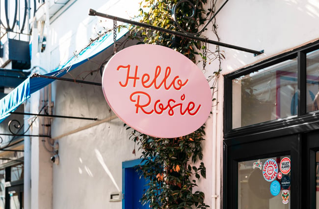A close up of a pink Hello Rosie hanging from an exterior wall.