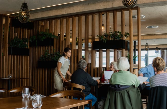 A staff member chatting to a group of people at a large dining table.