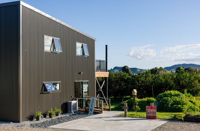Black building exterior of Hill Road and the orchard in the background.