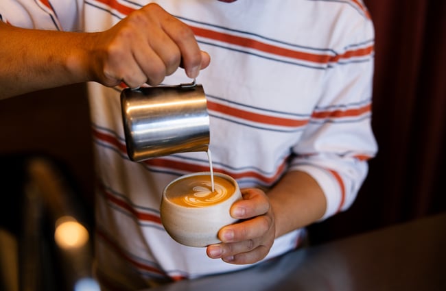 Barista in stripy top pouring a flat white with heart latte art
