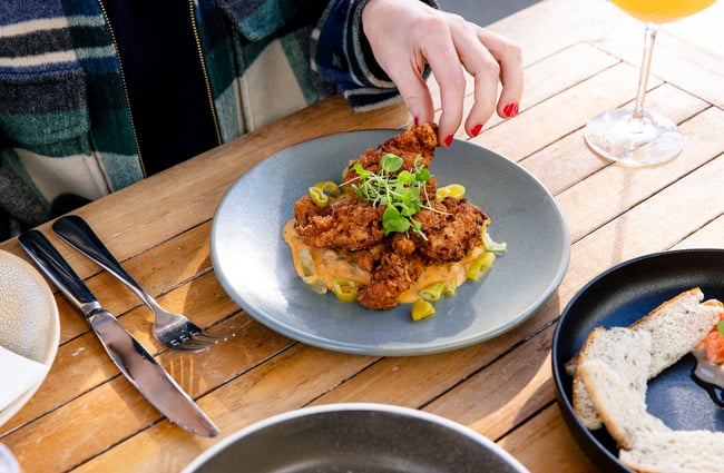 A hand reaching for fried chicken on a plate.
