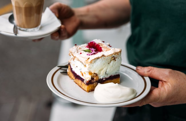 Waiter carrying a plate of pillowy Louise Cake and a cup of coffee