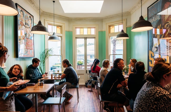 People sitting down eating and drinking inside villa style cafe in Petone