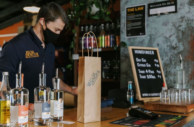 Gin bottles on the counter at Humdinger with a staff member standing behind at Humdinger Gin Distillery in Geraldine.