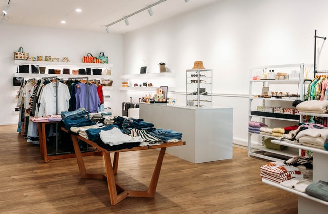 Contemporary fashion boutique with white shop counter surrounded by clothing on metal racks and jeans folded on timber tables