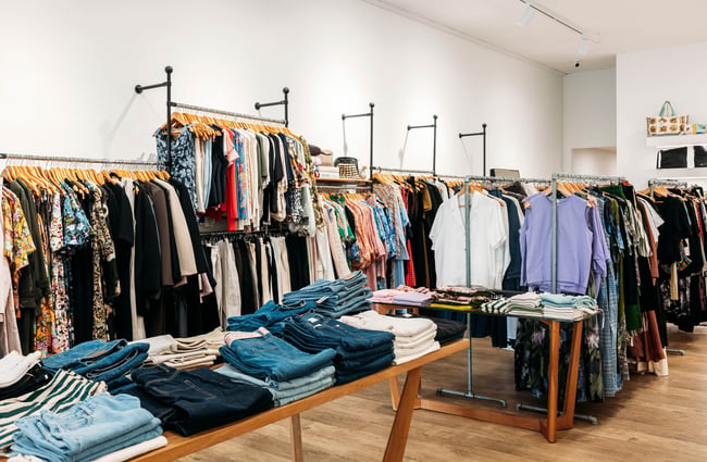 Fashion store fully stocked with women's clothing, featuring dresses and tops hanging up and a table with folded jeans in front