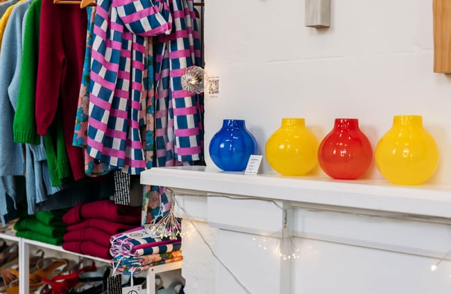 Colourful glass vases on shelf ledge next to a rack of colourful clothing