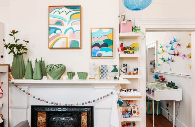 Colourful abstract art on wall above old fireplace with green vases on shelf ledge
