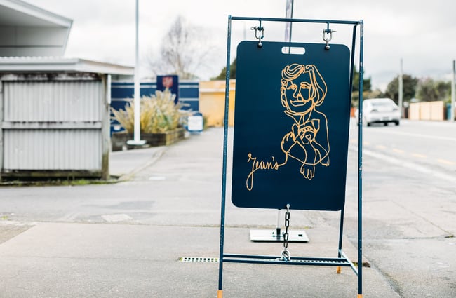 A dark blue footpath sign for Jean's cafe in Upper Hutt.