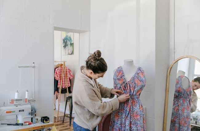 A female staff member tending to a colourful dress on a mannequin.