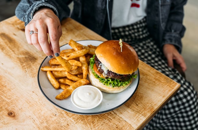 A hand reaching for a hot chip next to a burger.