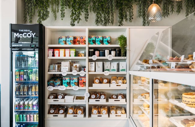 Baked goods on display next to a drinks fridge in a cafe.