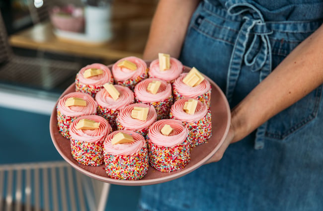 Hands holding a plate of sweet pink treats.