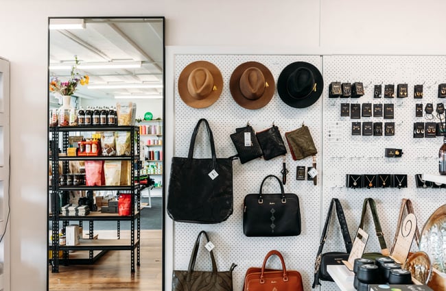 Various hats and different sized bags hanging on the wall next to a mirror at Journey & Co.