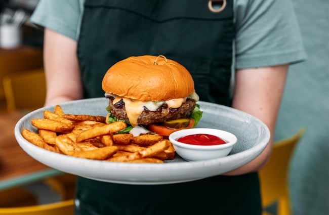 Cafe assistant holds a plate of burger and fries at Kōwhai Eatery.