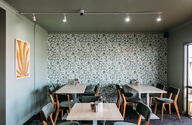 Colourful wallpaper on the wall behind several tables and chairs at Kōwhai Eatery.