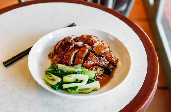 A close up of a plate of duck on thin noodles with steamed greens.