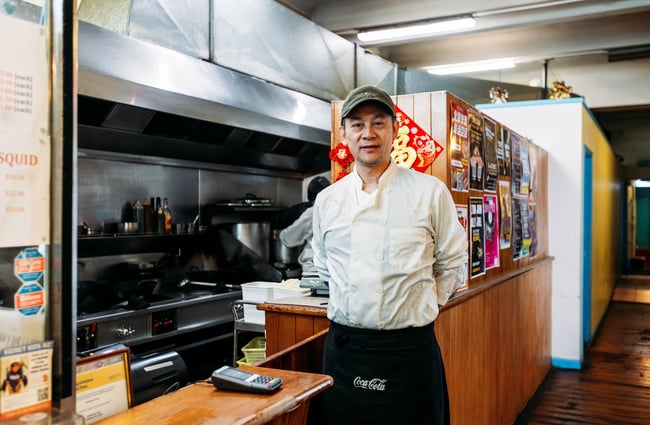 KC Cafe owner and namesake, Kom Fai Chan, stands in front of the kitchen.