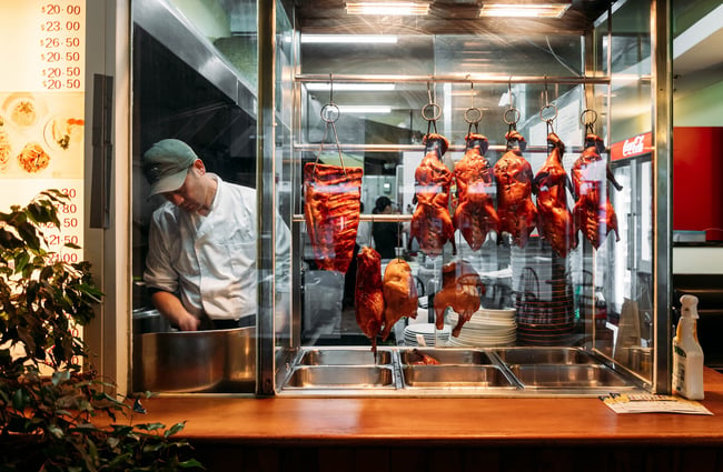Roast ducks hanging in a glass cabinet at the counter inside KC Cafe.