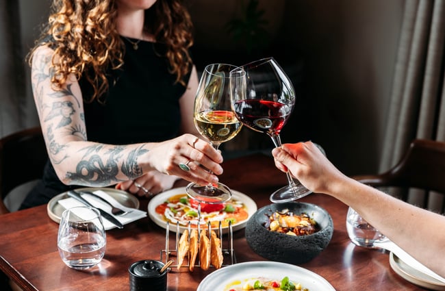 Customers doing a cheers with their wine glasses and food dishes on the table at KIKA.