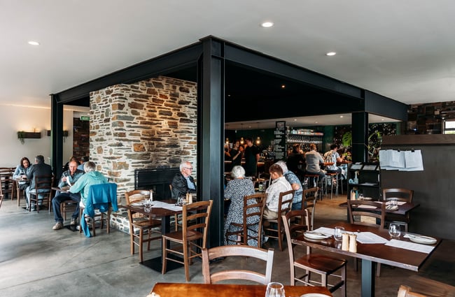 View of the dining area inside kika, framed by a large black steel frame and central stone full-height fireplace.